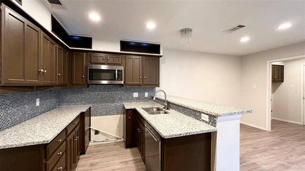 Kitchen featuring dark wood cabinetry, speckled stone-finish countertops, geometric tile backsplash, stainless steel microwave, and wood-finish flooring