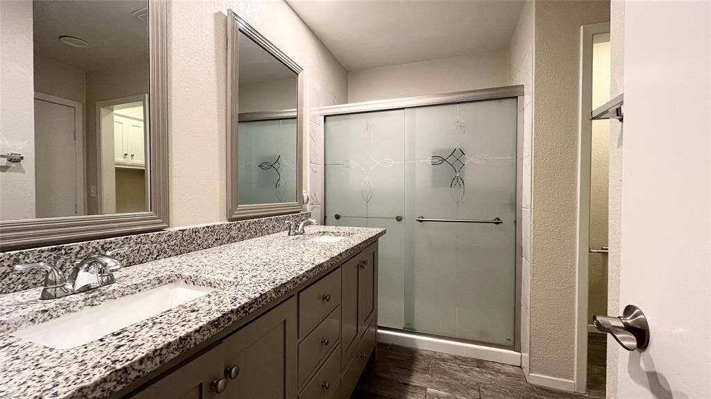 Dual-sink vanity with stone-finish countertop, framed wall mirrors, and shower enclosure with frosted glass doors and etched detailing