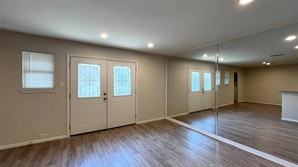 Double entry doors with decorative glass inserts, recessed lighting, wood-finish flooring, and a floor-to-ceiling mirrored wall
