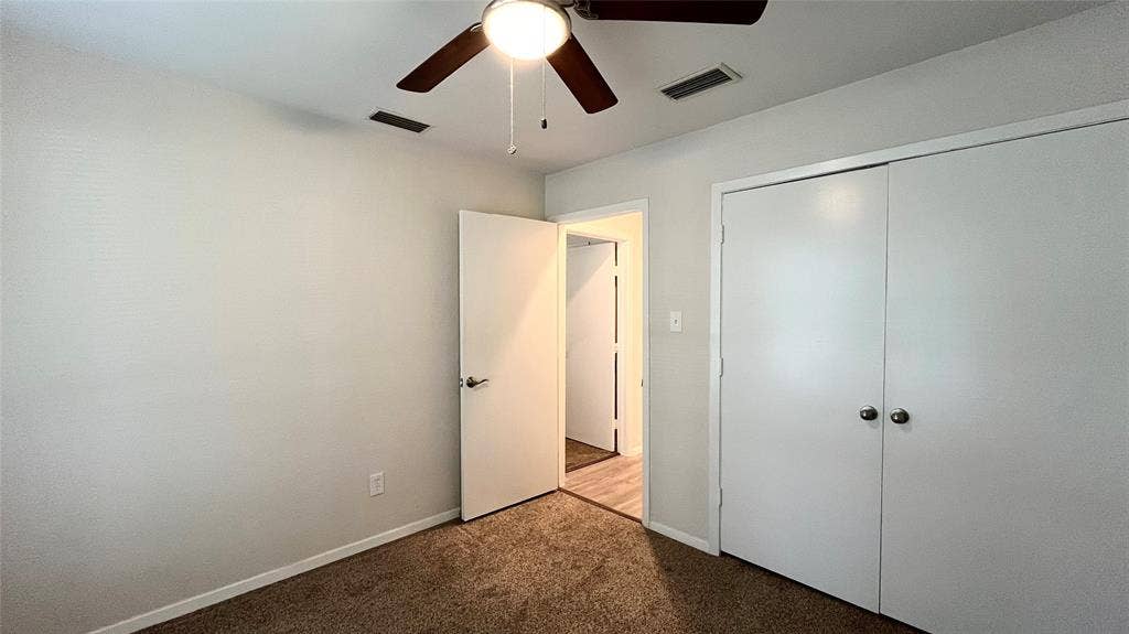 Neutral interior space featuring carpeting, a central ceiling fan with integrated lighting, and dual-panel closet doors