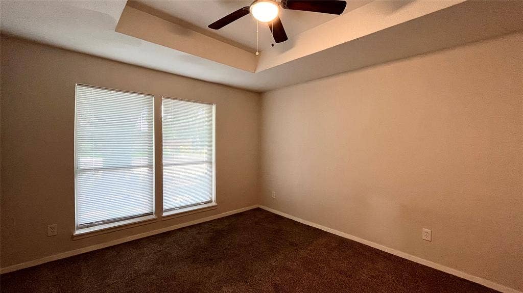 Room featuring a tray ceiling, ceiling fan with integrated lighting, dual windows with blinds, and wall-to-wall carpeting
