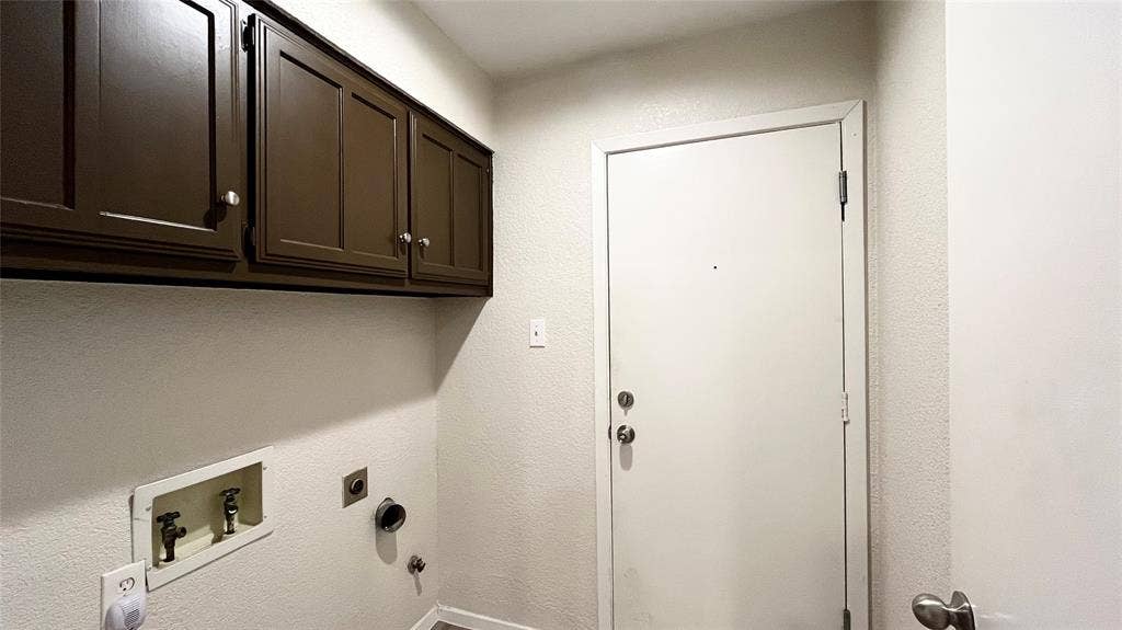Utility area featuring dark-finish upper cabinetry, integrated plumbing hookups, and a solid-core entry door with dual locking mechanisms