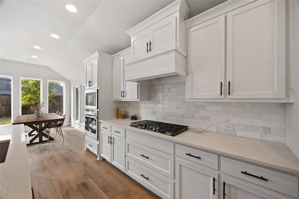 2820 Eccleston Street, Celina, TX 75009 Kitchen featuring white shaker-style cabinetry, a stone-tiled backsplash, integrated gas cooktop, built-in double oven, and wood-finish flooring