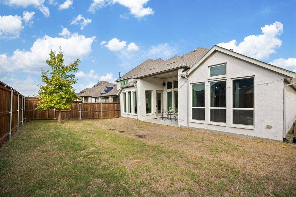 2820 Eccleston Street, Celina, TX 75009 Rear exterior featuring a white-painted brick facade, covered patio, multiple tall windows, and a wood privacy fence enclosing the backyard