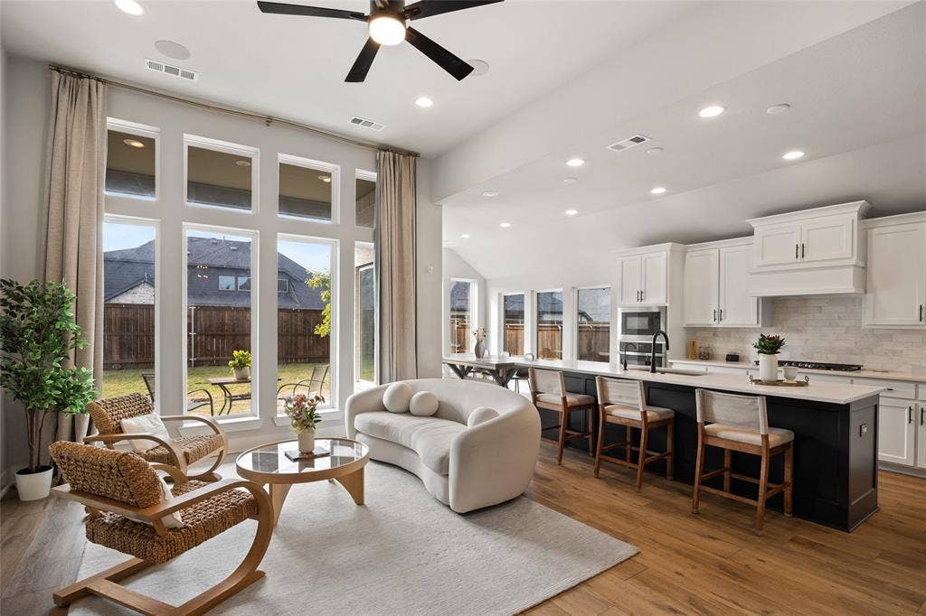 2820 Eccleston Street, Celina, TX 75009 Open-concept living space featuring high ceilings with recessed lighting, oversized windows, wood-finish flooring, and a kitchen with white cabinetry and a contrasting center island
