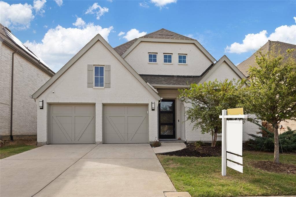 2820 Eccleston Street, Celina, TX 75009 Light-colored brick exterior with a multi-gable roofline, two-car garage with carriage-style doors, and contemporary glass-panel front entry door