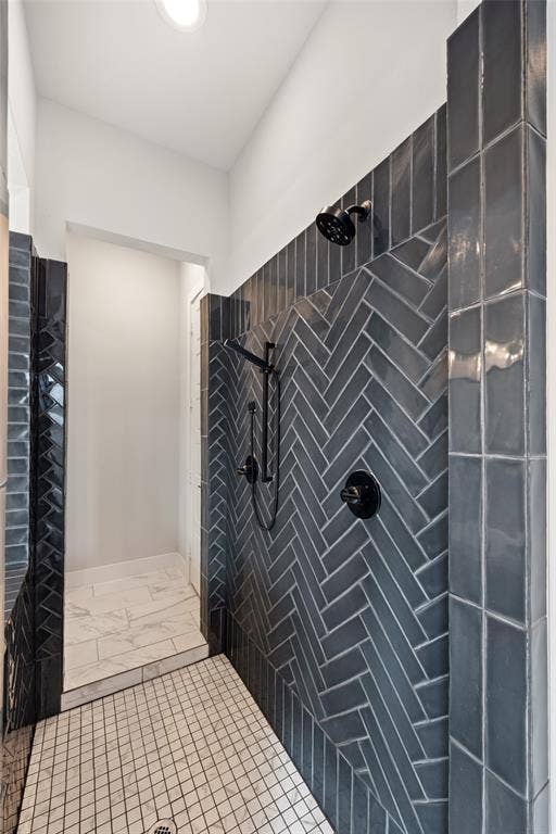 2820 Eccleston Street, Celina, TX 75009 Walk-in shower featuring charcoal-toned subway tile arranged in a herringbone pattern, matte black wall-mounted shower fixtures, handheld sprayer, and stone-look floor tiling