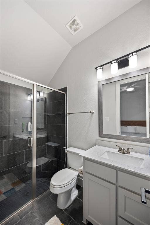 2820 Eccleston Street, Celina, TX 75009 Bathroom featuring vaulted ceilings, a vanity with a stone-top integrated sink, a framed vanity mirror, and a walk-in shower with dark tile surround and a glass door