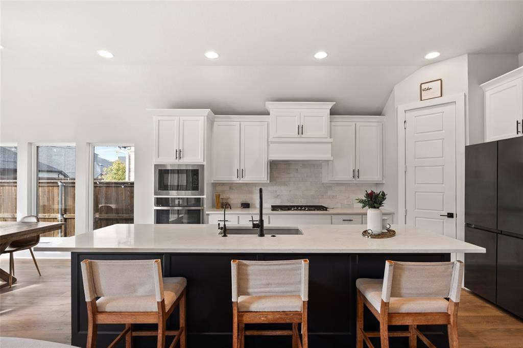 2820 Eccleston Street, Celina, TX 75009 Kitchen featuring white shaker cabinetry, a contrasting dark kitchen island with a stone countertop, built-in wall oven and microwave, stone tile backsplash, and recessed lighting