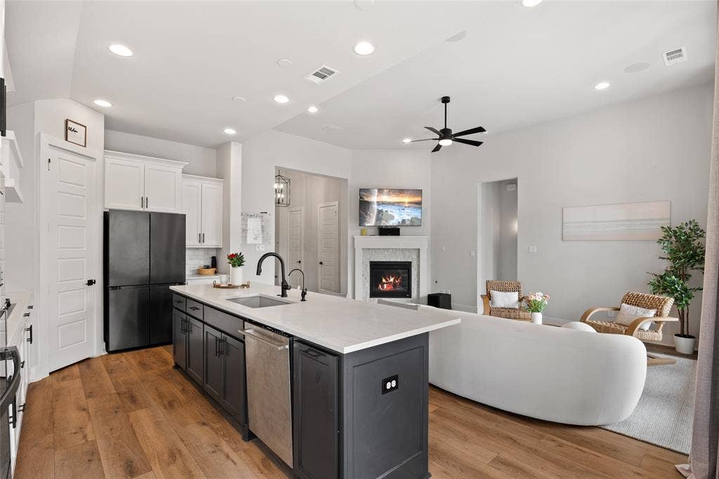 2820 Eccleston Street, Celina, TX 75009 Kitchen featuring a two-tone island with a light-colored countertop, recessed lighting, wood-finish flooring, and a fireplace with a decorative surround