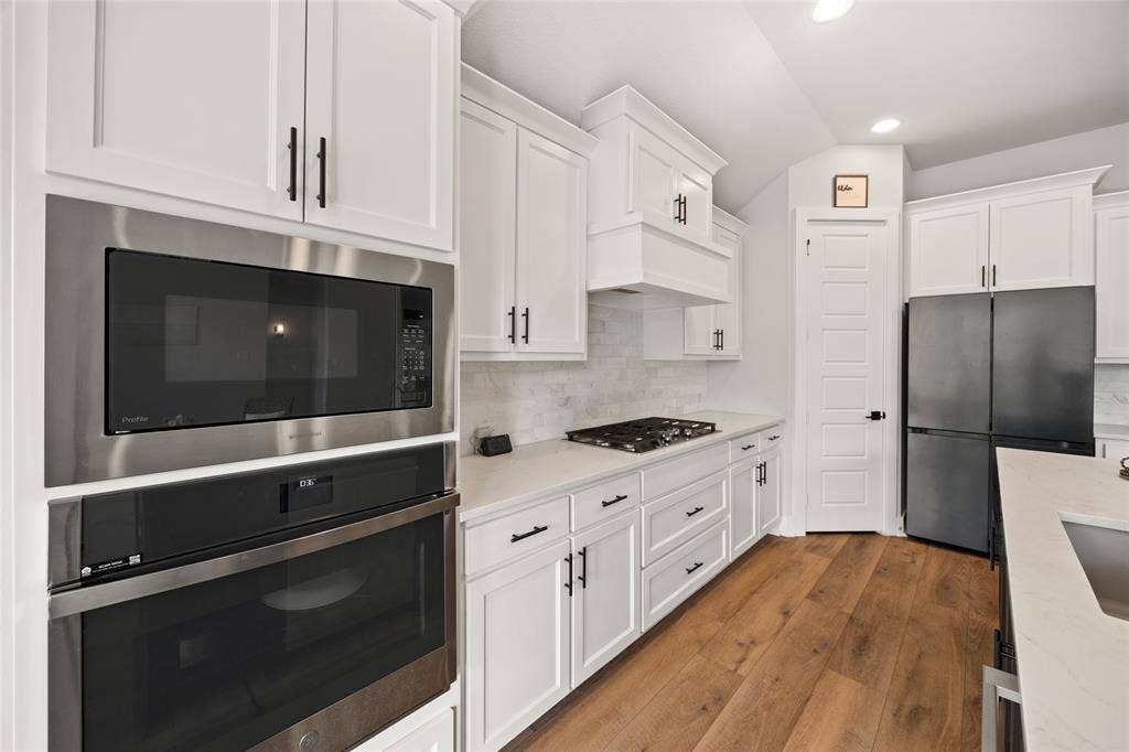 2820 Eccleston Street, Celina, TX 75009 Kitchen featuring white shaker-style cabinetry, stainless steel built-in double ovens and microwave, quartz countertops, gas cooktop, and wood-finish flooring