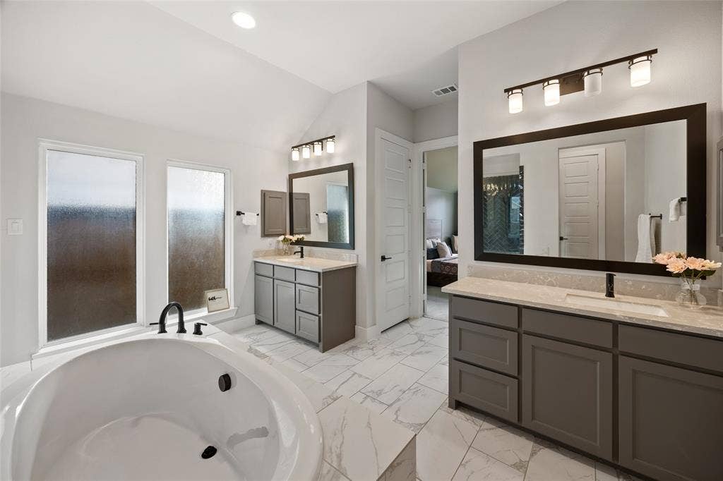 2820 Eccleston Street, Celina, TX 75009 Dual vanities with shaker-style cabinetry, stone-finish countertops, tile flooring, freestanding soaking tub, and contemporary wall-mounted light fixtures