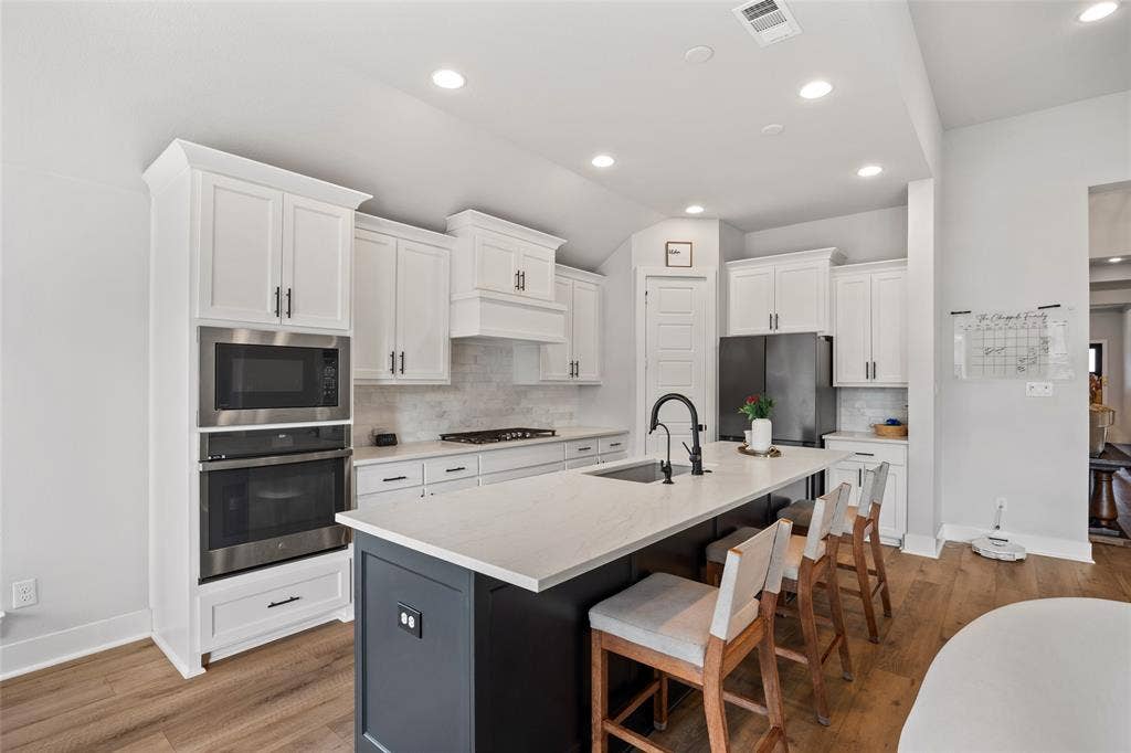 2820 Eccleston Street, Celina, TX 75009 Kitchen featuring white shaker-style cabinetry, an expansive center island with a stone countertop, recessed lighting, stainless steel built-in double ovens, and wood-finish flooring