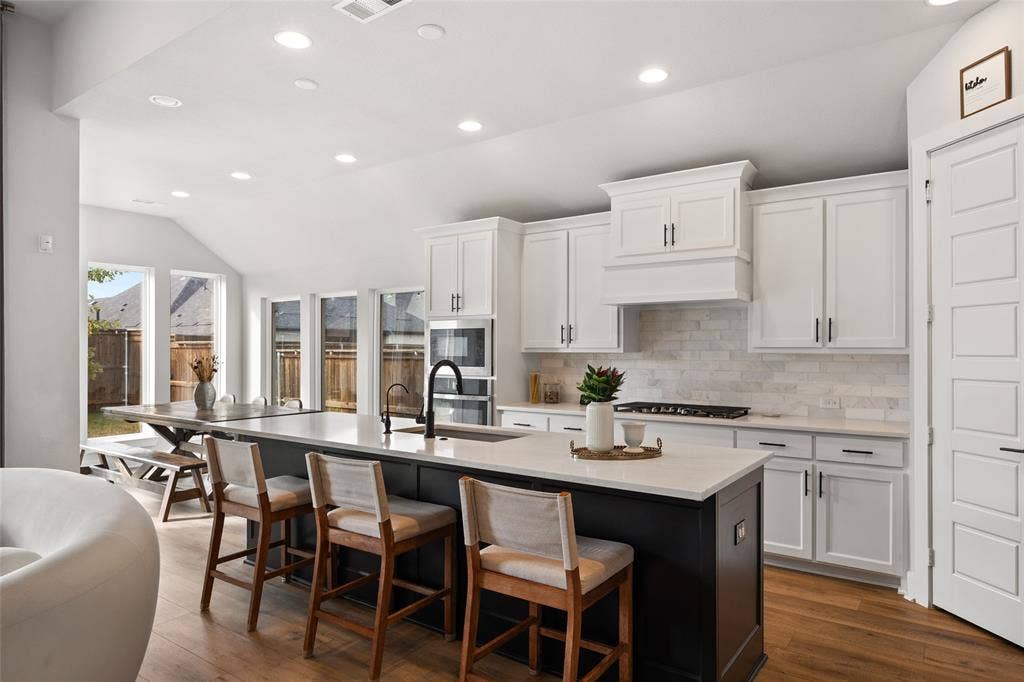 2820 Eccleston Street, Celina, TX 75009 Kitchen featuring white shaker-style cabinetry, dark contrast kitchen island with a light-toned countertop, subway tile backsplash, built-in double oven, and wood-finish flooring