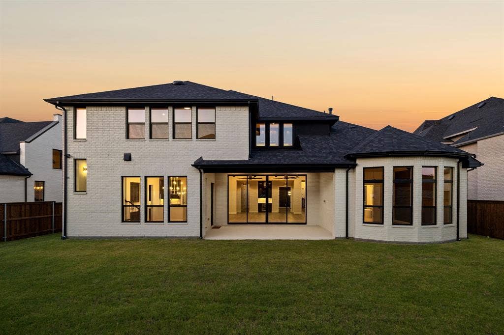 Exterior facade featuring white brick masonry, black window framing, architectural shingle roofing, a covered concrete patio, and a turret-style bay window