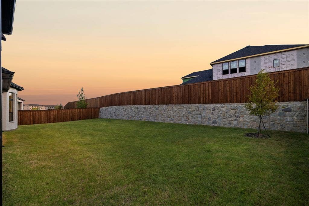 Expansive backyard featuring a natural stone retaining wall, full-perimeter wood fencing, and established lawn