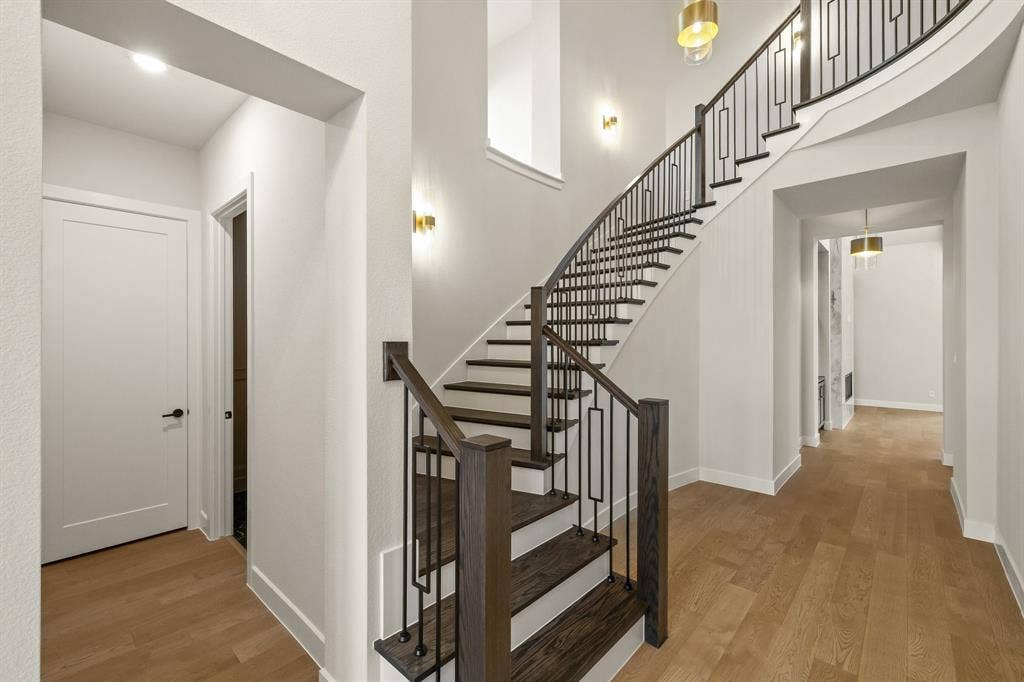 Curved staircase featuring stained wood-finish treads, custom metal railings, and wood-finish flooring