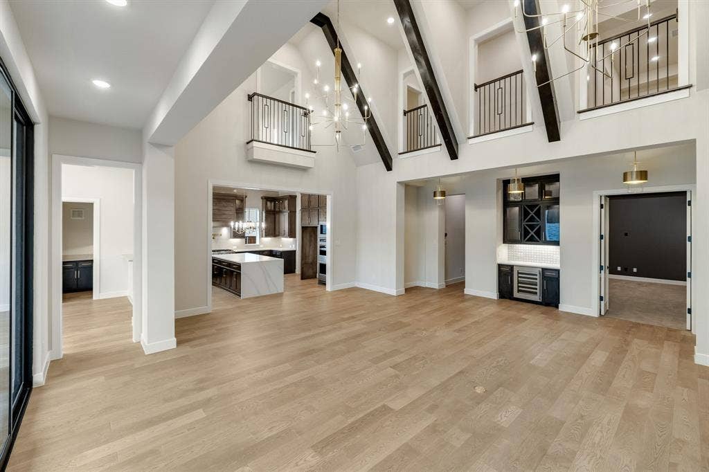 Vaulted ceilings featuring exposed timber beams, wood-finish flooring, a built-in wet bar with wine refrigeration, multi-level balcony railings, and recessed lighting