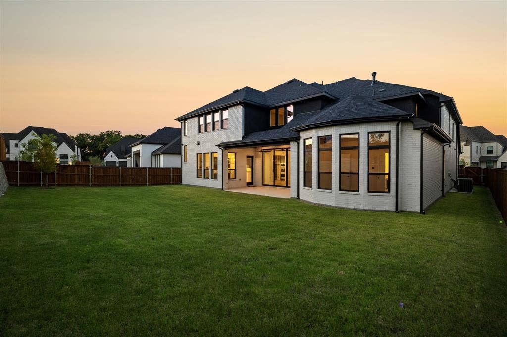 Multi-story residence featuring white brick exterior, black-trimmed windows, expansive rear lawn, and a covered concrete patio