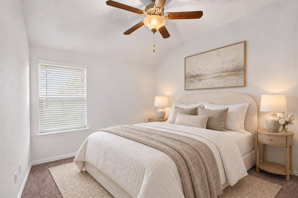 Neutral-toned interior featuring vaulted ceilings, a central ceiling fan with integrated lighting, carpeted flooring, and a single-pane window with horizontal blinds