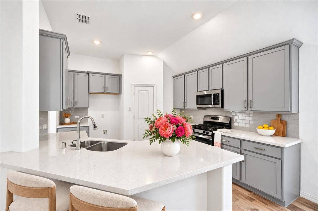 Kitchen featuring shaker-style grey cabinetry, solid surface countertops, a white subway tile backsplash, stainless steel appliances