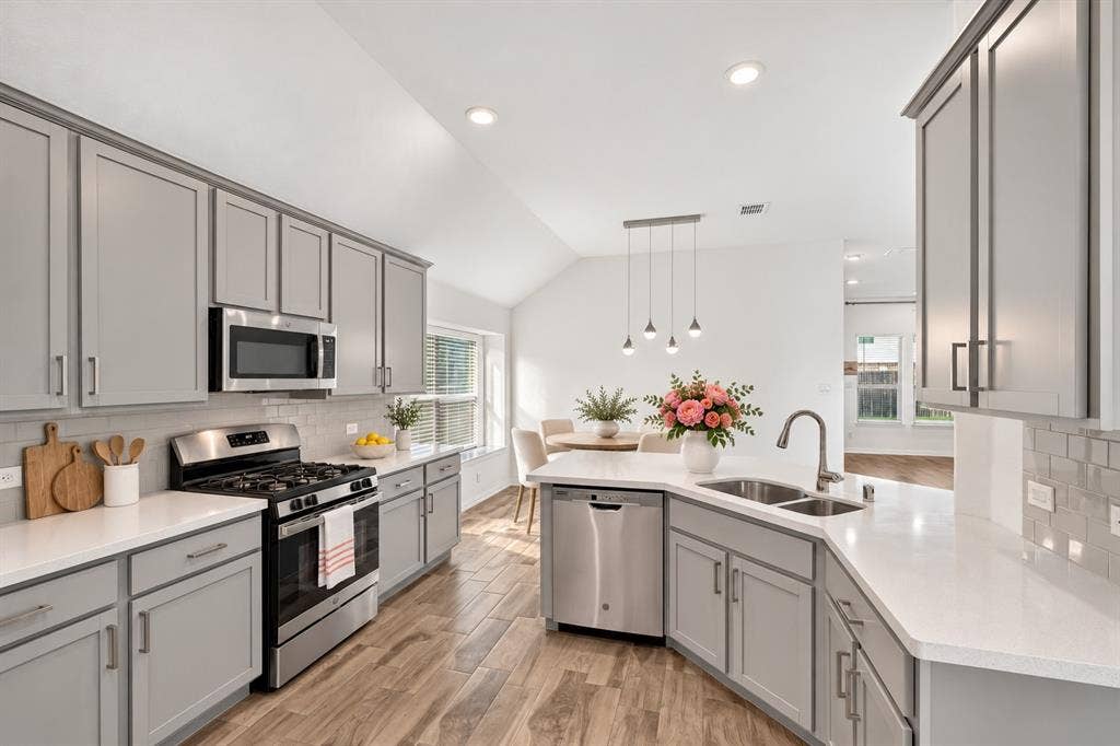 Kitchen featuring shaker-style cabinetry, solid surface countertops, a subway tile backsplash, stainless steel appliances, and wood-finish flooring under a vaulted ceiling