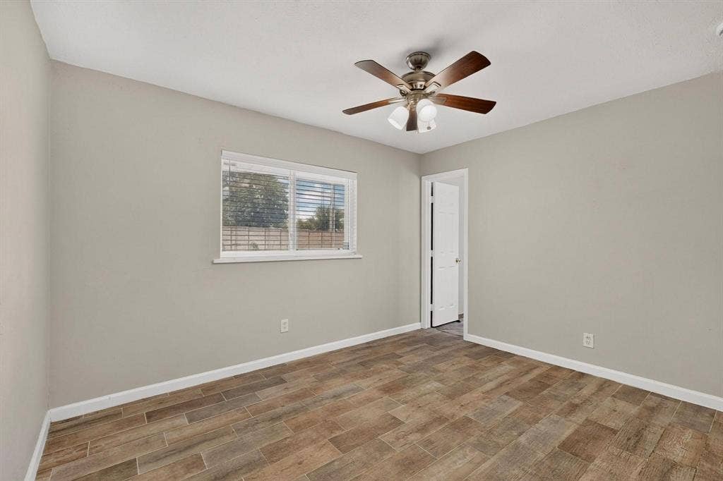 501 Starling Drive, Mesquite, TX 75149 Spacious primary bedroom showcasing a ceiling fan, a wide window, hardwood floors and an en suite bath, inviting comfort and style.