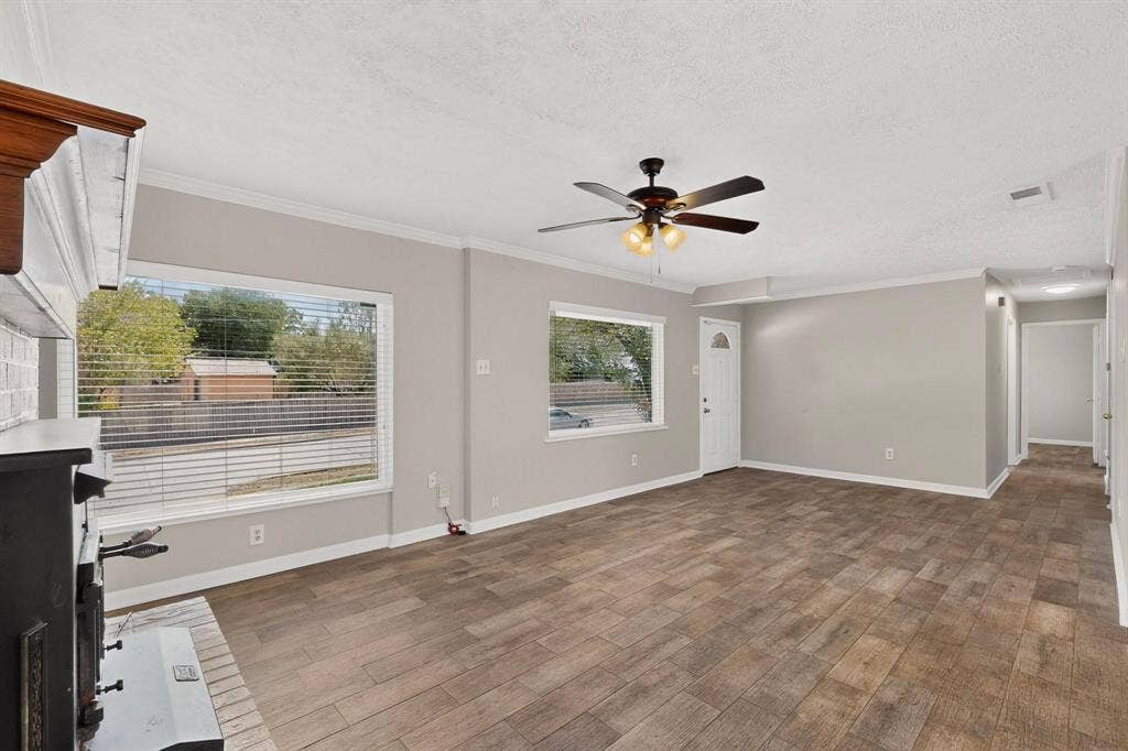 501 Starling Drive, Mesquite, TX 75149 A bright living room featuring hardwood floors, a fireplace, a ceiling fan and wide windows, creating a spacious and airy atmosphere.