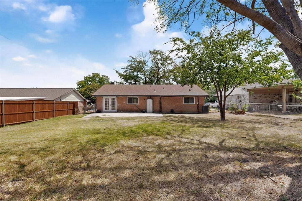 501 Starling Drive, Mesquite, TX 75149 A grassy yard with a patio and a lush tree enclosed by a wooden fence, inviting a sense of tranquility.