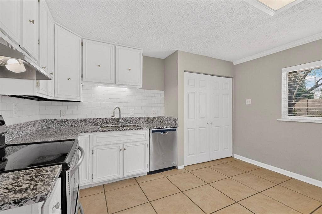 501 Starling Drive, Mesquite, TX 75149 A contemporary kitchen showcasing a wide window, white cabinetry and tile flooring, perfect for meal preparation and family gatherings.