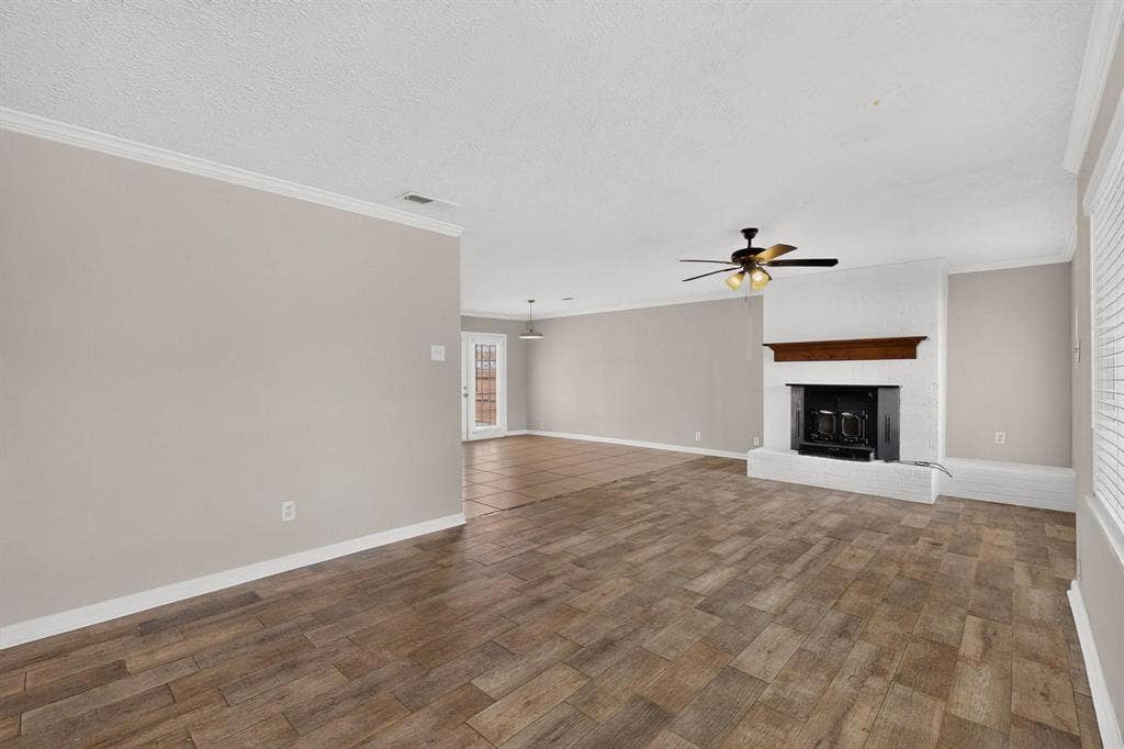 501 Starling Drive, Mesquite, TX 75149 A spacious living room featuring hardwood floors, a fireplace and a ceiling fan, ready for new furnishings and decor.