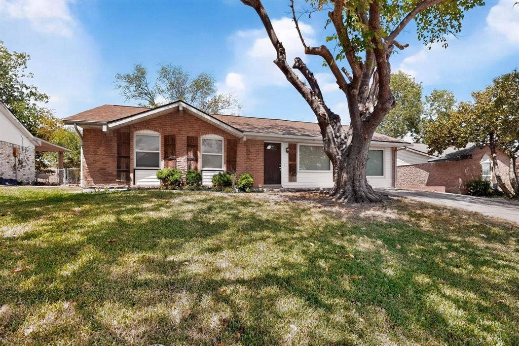 501 Starling Drive, Mesquite, TX 75149 A charming brick home set in a large yard, featuring a green yard and a large tree for shade and beauty.