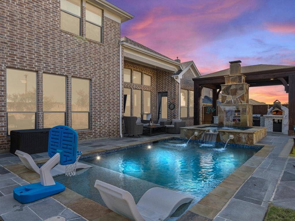 1506 Hennessey Drive, Allen, TX 75013 View of swimming pool featuring an outdoor stone fireplace, an outdoor kitchen, a patio area, and a pool with connected hot tub