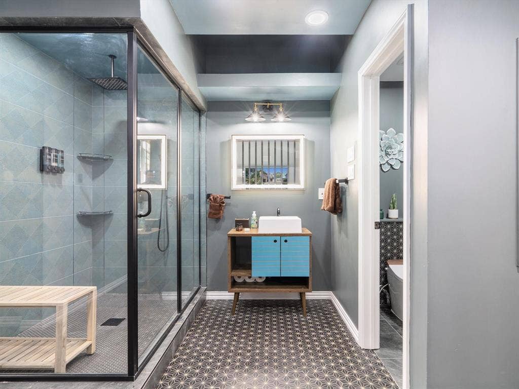 1506 Hennessey Drive, Allen, TX 75013 Ensuite Bathroom – In-Law SuiteSecond-floor full ensuite: walk-in glass shower with rain head, gray tile surround/floors, wood vanity with blue cabinetry and vessel sink, recessed lights, wooden bench. Modern & private.