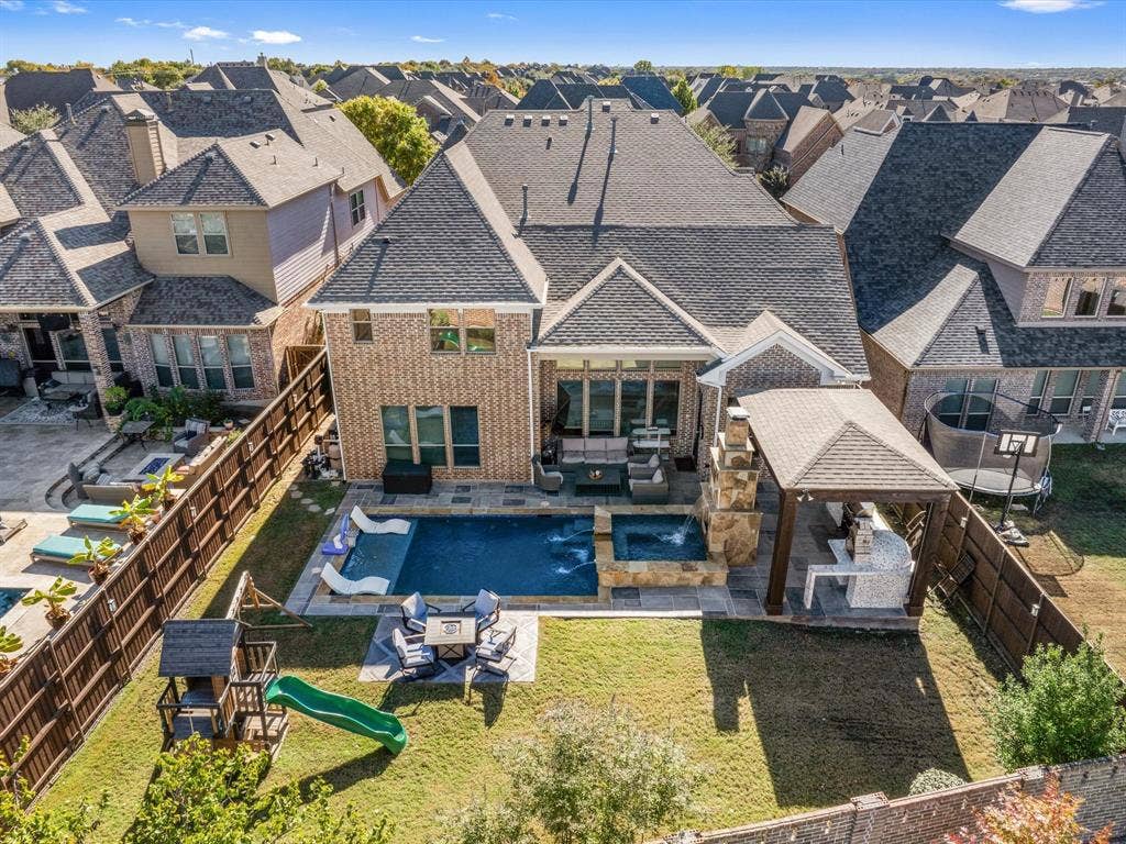 1506 Hennessey Drive, Allen, TX 75013 Backyard aerial view of a premium Allen home with a spacious, fully fenced backyard featuring a resort-style pool, attached spa, multiple covered patios, outdoor seating with fire features, playset, mature landscaping, and ample entertaining space.