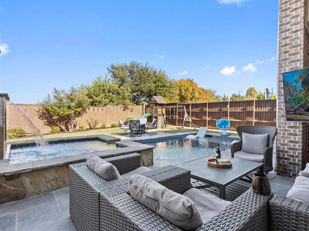 1506 Hennessey Drive, Allen, TX 75013 Outdoor living features a stunning backyard oasis with a sparkling swimming pool and attached hot tub, a spacious patio with wicker sectional seating and a coffee table, a covered hangout area, a fenced yard with a playset, mature trees, and a serene fountain. Perfect for relaxation and family fun.