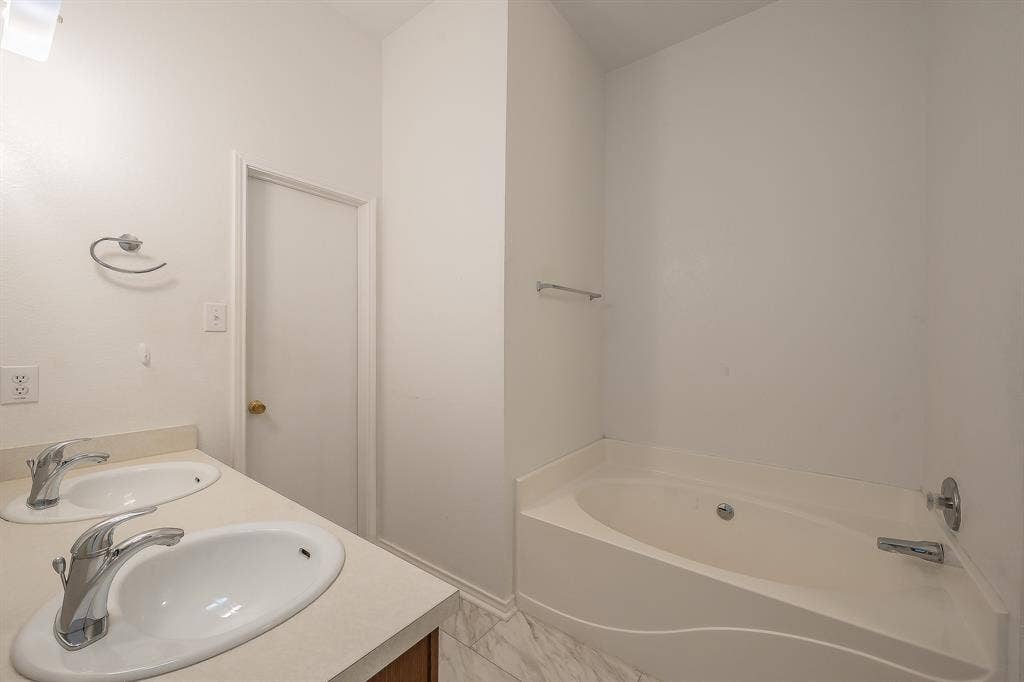 6833 Bluff View Drive, Watauga, TX 76137 Dual-sink vanity with a solid-surface countertop and chrome-finish faucets, featuring an integrated soaking tub and stone-pattern flooring