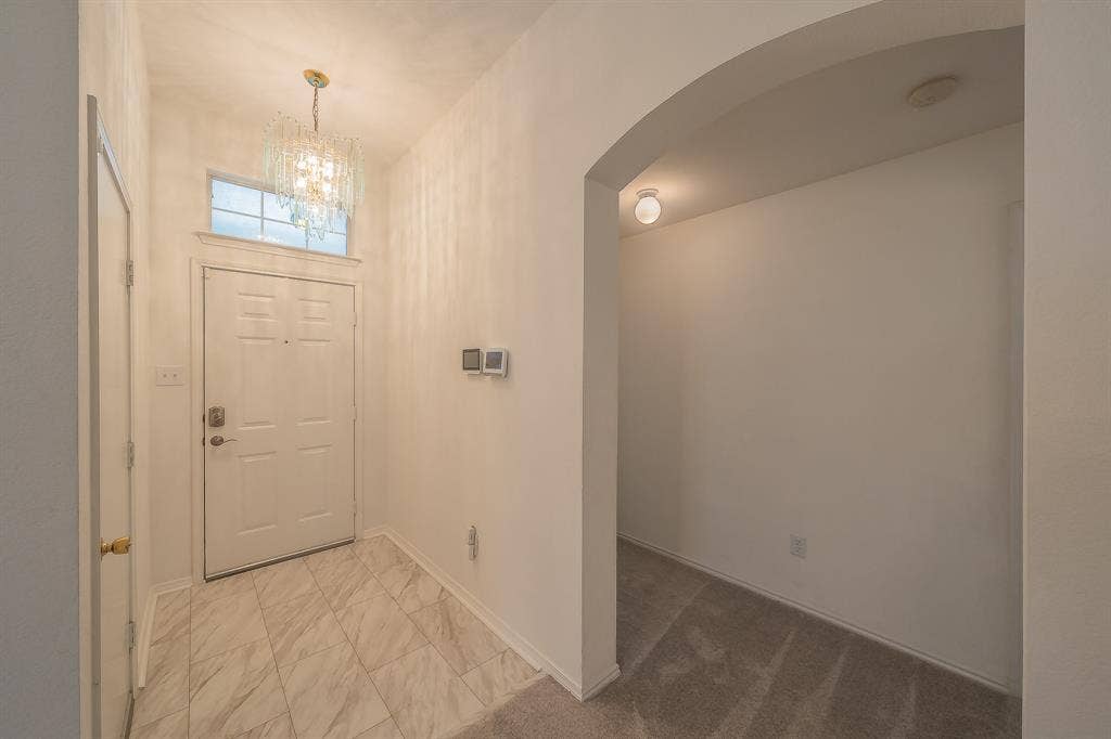 6833 Bluff View Drive, Watauga, TX 76137 Entryway featuring high ceilings, a crystal-style chandelier, a transom window above the door, stone-finish tile flooring, and an arched doorway