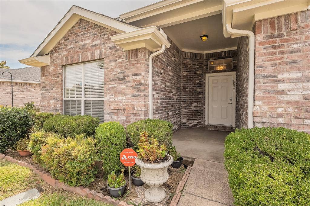 6833 Bluff View Drive, Watauga, TX 76137 Multi-toned brick exterior featuring a covered entryway, concrete front porch, transom window above the entry door, and manicured shrubbery