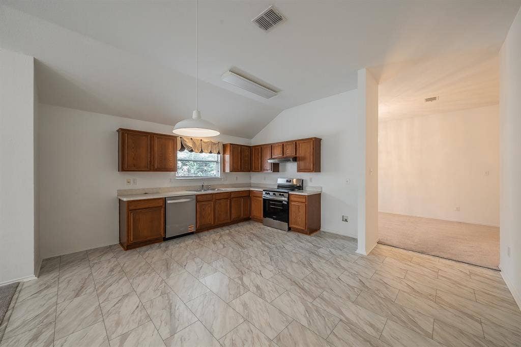 6833 Bluff View Drive, Watauga, TX 76137 Kitchen featuring wood cabinetry, stone-finish tile flooring, a stainless steel dishwasher, a slide-in range, and a vaulted ceiling with a pendant light fixture