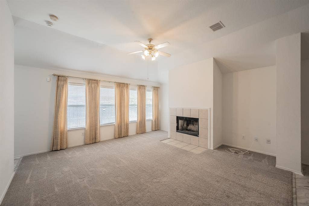 6833 Bluff View Drive, Watauga, TX 76137 Living area featuring vaulted ceilings, a fireplace with neutral tile surround and hearth, carpeted flooring, and multiple windows