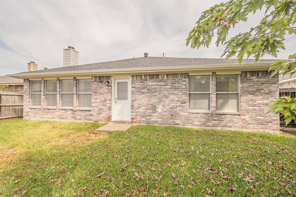 6833 Bluff View Drive, Watauga, TX 76137 Multi-tone brick exterior featuring a single-story profile, rear access door, shingle roof, two masonry chimneys, and multiple windows with horizontal blinds