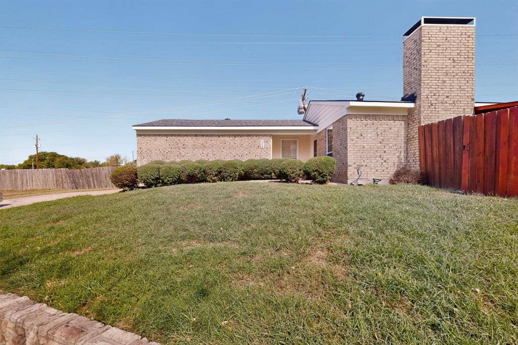2228 Bunker Hill Drive, Carrollton, TX 75006 Single-story brick exterior featuring a prominent masonry chimney, stone landscape edging, and mature shrubs
