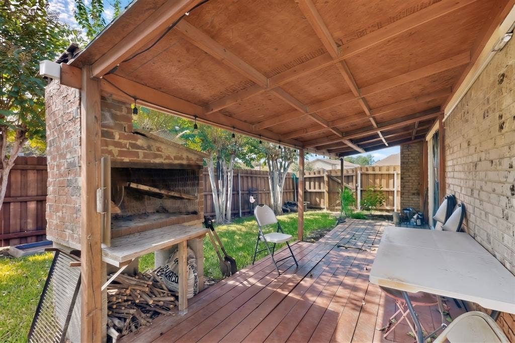 2228 Bunker Hill Drive, Carrollton, TX 75006 Covered wooden deck featuring a built-in masonry outdoor fireplace, exposed wood-beam ceiling, and brick exterior wall