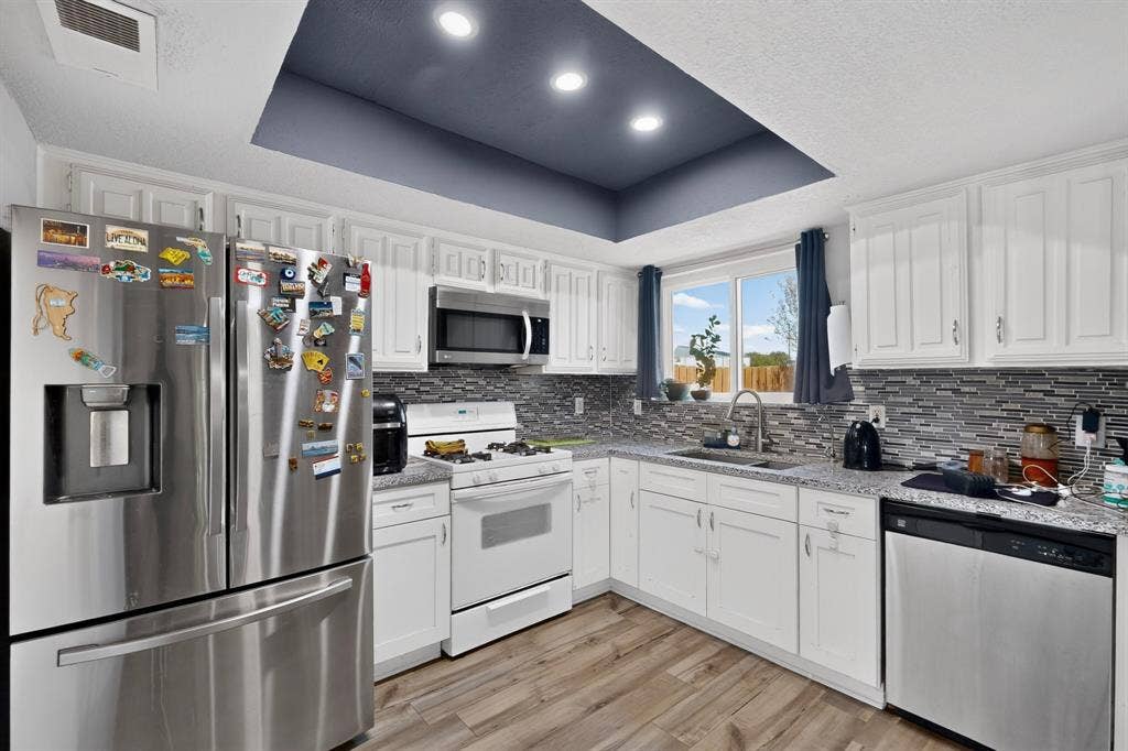 2228 Bunker Hill Drive, Carrollton, TX 75006 Kitchen featuring white cabinetry, stone-finish countertops, mosaic tile backsplash, recessed tray ceiling, and wood-finish flooring