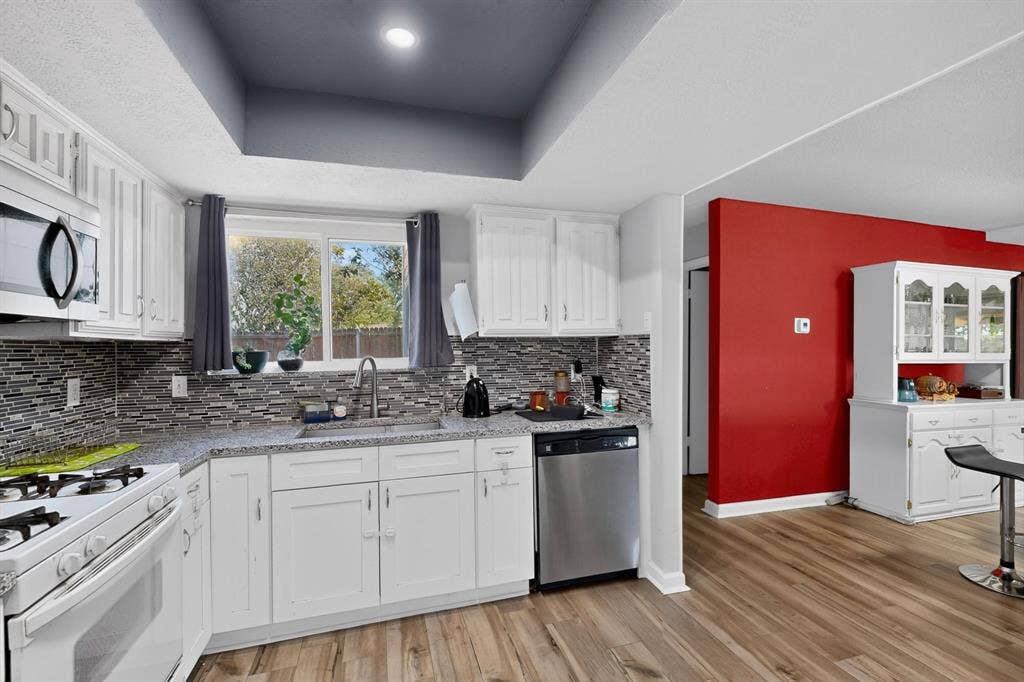 2228 Bunker Hill Drive, Carrollton, TX 75006 Kitchen featuring white cabinetry, stone-finish countertops, multi-toned tile backsplash, stainless steel dishwasher, and wood-finish flooring