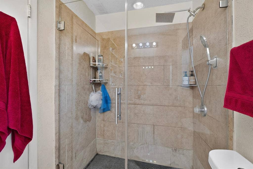 2228 Bunker Hill Drive, Carrollton, TX 75006 Walk-in shower featuring floor-to-ceiling neutral tile, glass enclosure, ceiling-mounted rainfall showerhead, and handheld sprayer