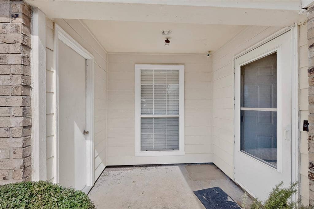 2228 Bunker Hill Drive, Carrollton, TX 75006 Covered entryway featuring light-toned horizontal siding, brick facade accents, a multi-pane window with blinds, and an exterior storage closet door