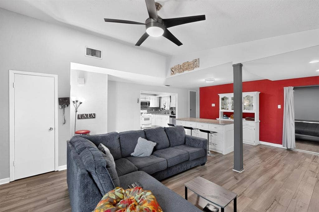 2228 Bunker Hill Drive, Carrollton, TX 75006 Vaulted ceilings with an integrated matte black ceiling fan, wood-finish flooring, and a central kitchen island featuring white cabinetry and stone-finish countertops