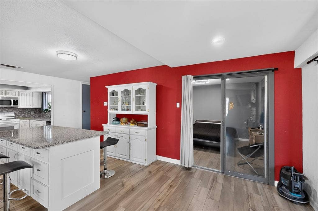 2228 Bunker Hill Drive, Carrollton, TX 75006 Kitchen featuring a stone-topped central island, built-in white cabinetry, wood-finish flooring, and sliding glass doors